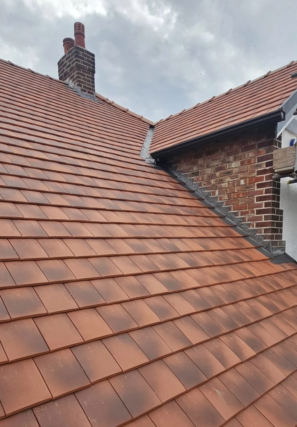 Clay plain tile roof with stepped lead flashing against brickwork and a chimney stack