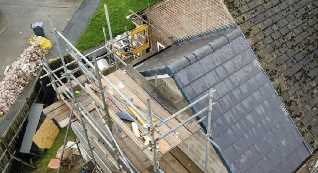 Extension roof from above with new slate-grey tiles and scaffold boards alongside