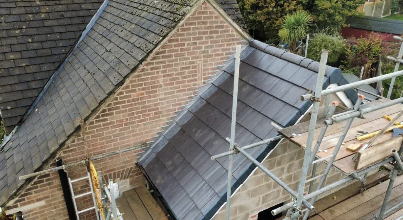 New tiled extension roof with dry verge joined to an older slate roof, scaffold in place