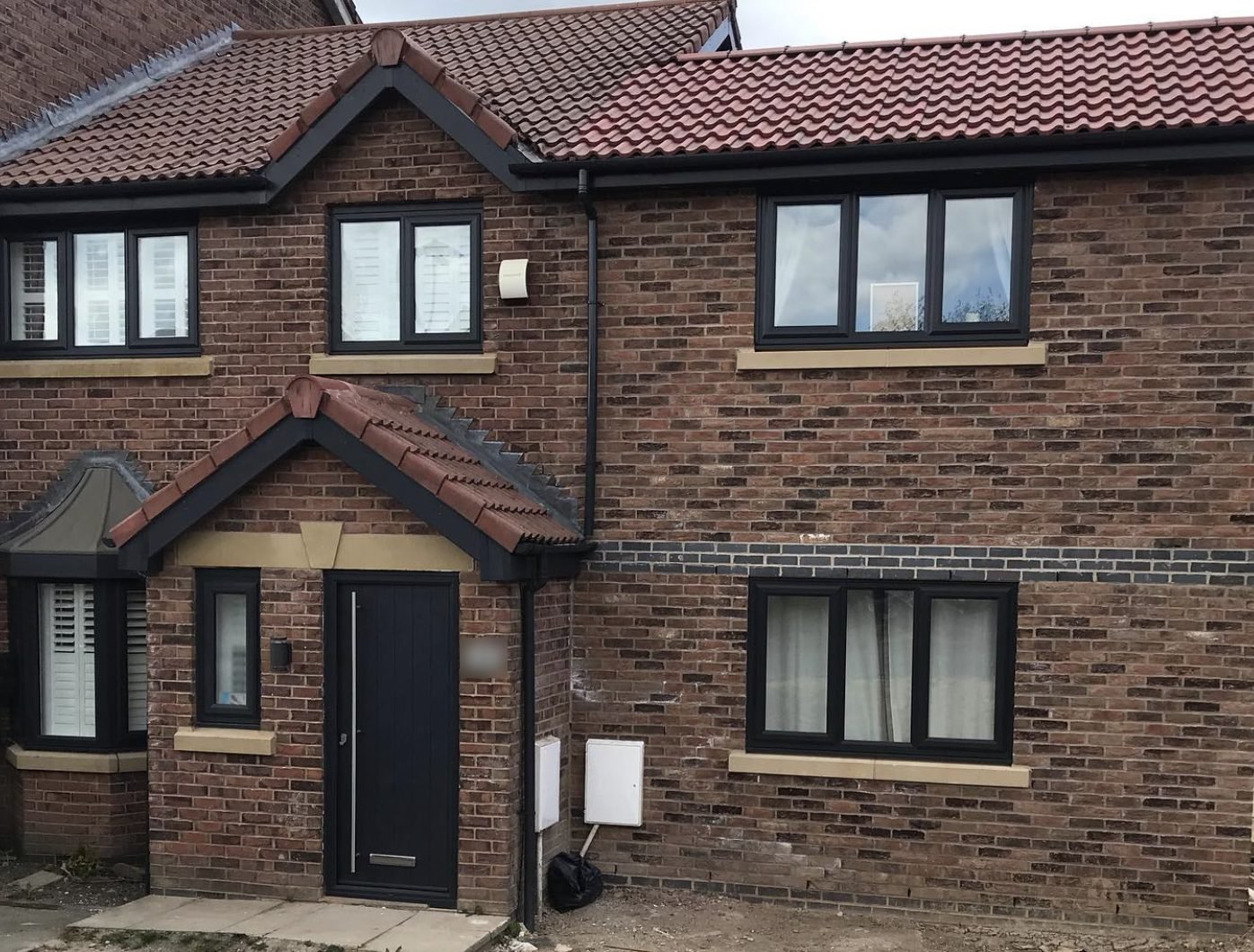Red tiled porch and main roof with black fascias and guttering on a brick house